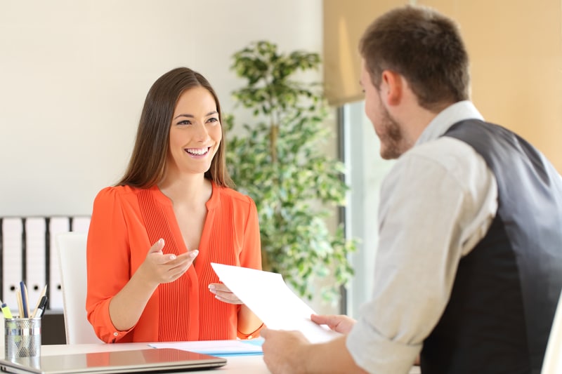Smiling woman handing off her resume to a hiring manager at an interview.
