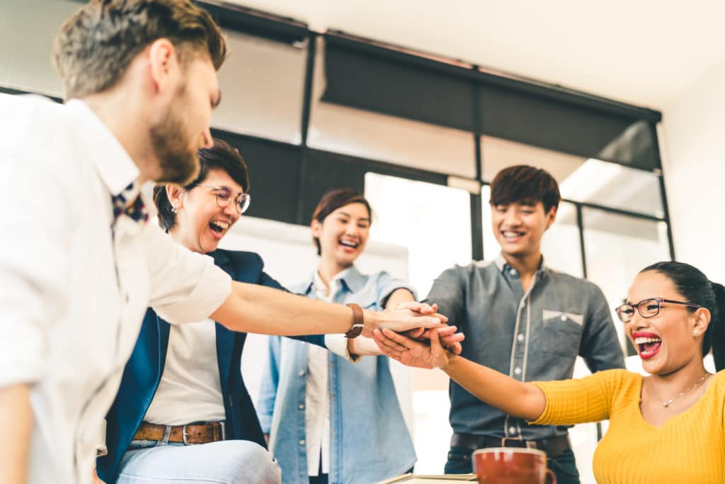 Group of workers smiling and putting their hands in the middle to celebrate.