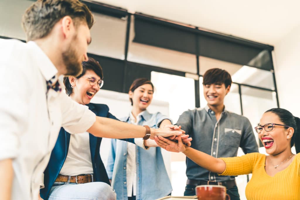 Group of workers smiling and putting their hands in the middle to celebrate.