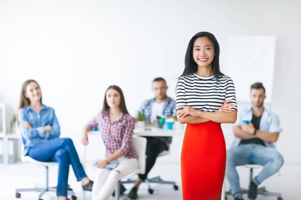 Woman wearing a red skirt standing in front of a room full of people.
