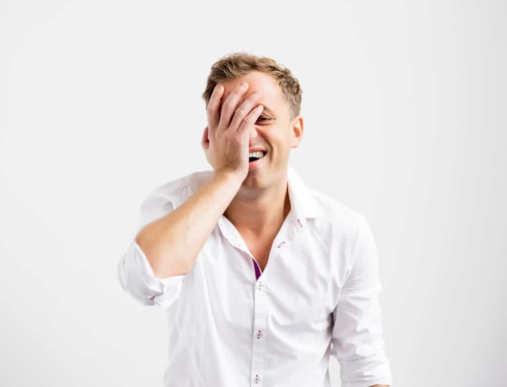 Man smiling and putting his hand to his face in embarrassment.