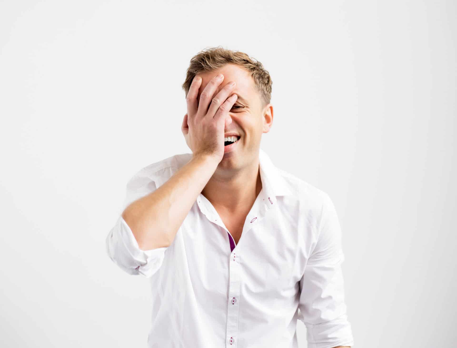 Man smiling and putting his hand to his face in embarrassment.