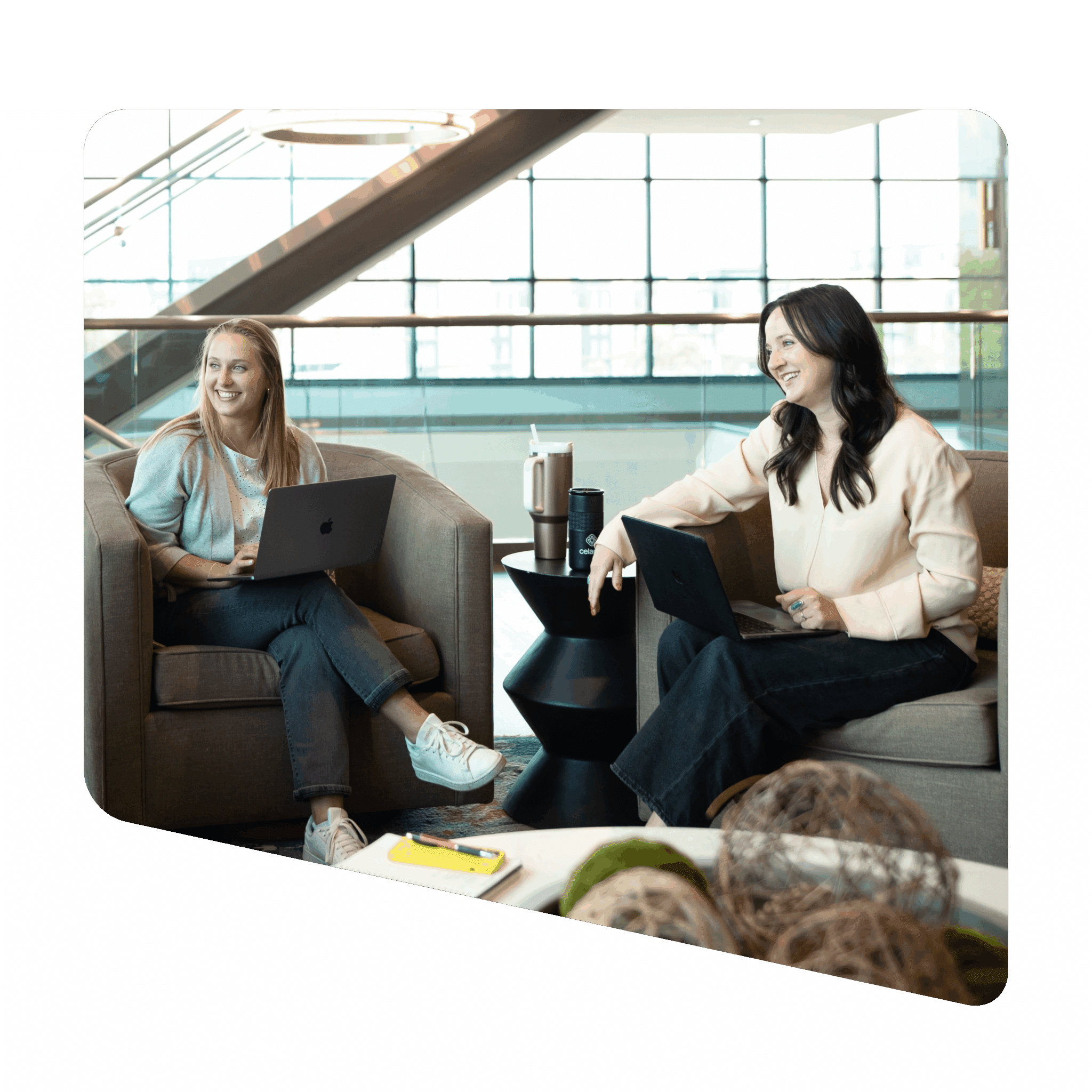 Two professional women collaborating in modern office lounge with laptops